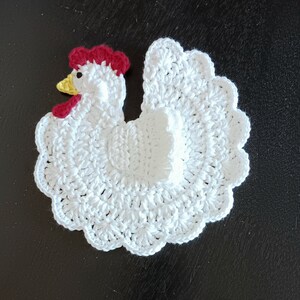 May include: White crocheted chicken with a red comb and yellow beak. The chicken is a decorative item, possibly a kitchen towel or a coaster.