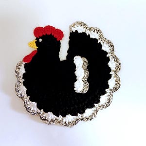 May include: A black crocheted chicken with a red comb and white and silver trim. The chicken is a decorative item.