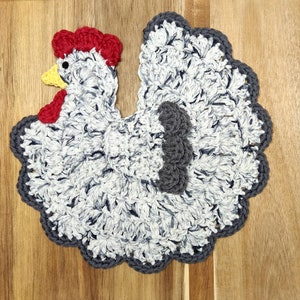 May include: A crocheted gray and white chicken with a red comb and yellow beak. The chicken is a kitchen pot holder.