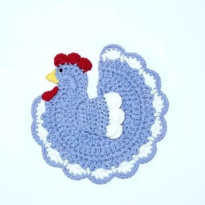 May include: A crocheted lavender-colored chicken with a red comb and white accents. The chicken is a kitchen dishcloth or pot holder.