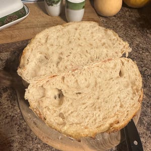 K&ouml;nnte beinhalten: Nahaufnahme eines frisch gebackenen Brotlaibs, der in zwei H&auml;lften geschnitten ist und eine hellbraune, luftige Krume mit gro&szlig;en L&ouml;chern zeigt. Das Brot liegt auf einem Holzbrett.