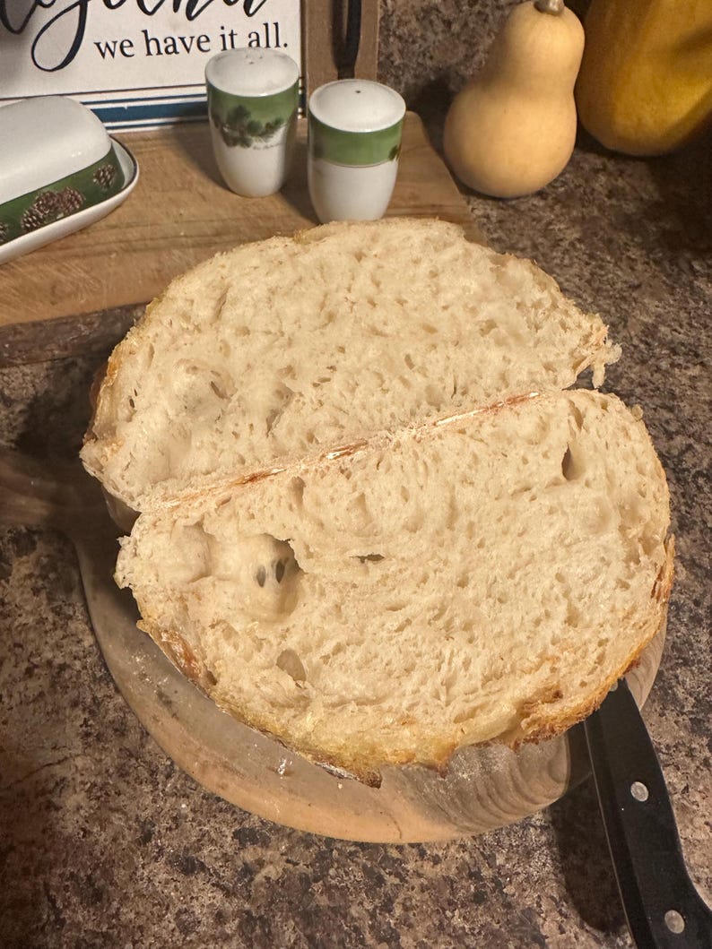 K&ouml;nnte beinhalten: Nahaufnahme eines frisch gebackenen Brotlaibs, der in zwei H&auml;lften geschnitten ist und eine hellbraune, luftige Krume mit gro&szlig;en L&ouml;chern zeigt. Das Brot liegt auf einem Holzbrett.