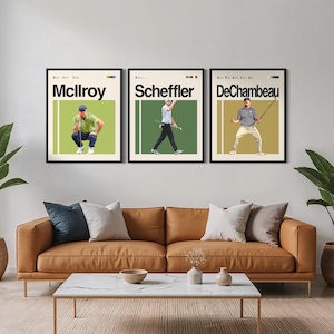 Puede incluir: Tres láminas enmarcadas de arte de golf con McIlroy, Scheffler y DeChambeau. Cada lámina tiene un fondo beige con una imagen de golfista y el nombre en letras negras en negrita. Las láminas se muestran encima de un sofá de cuero marrón.