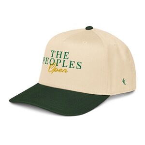 May include: A cream-coloured baseball cap with a dark green brim. The cap features the text "THE PEOPLES Open" in green and gold embroidery. A small logo is on the side. The cap is a stylish accessory.