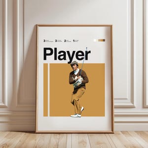 May include: Framed art print featuring a golfer in a brown sweater and khaki pants, holding a golf club. The word "Player" is in bold black letters. The background is a mustard yellow color with white vertical lines. The print is in a wooden frame.