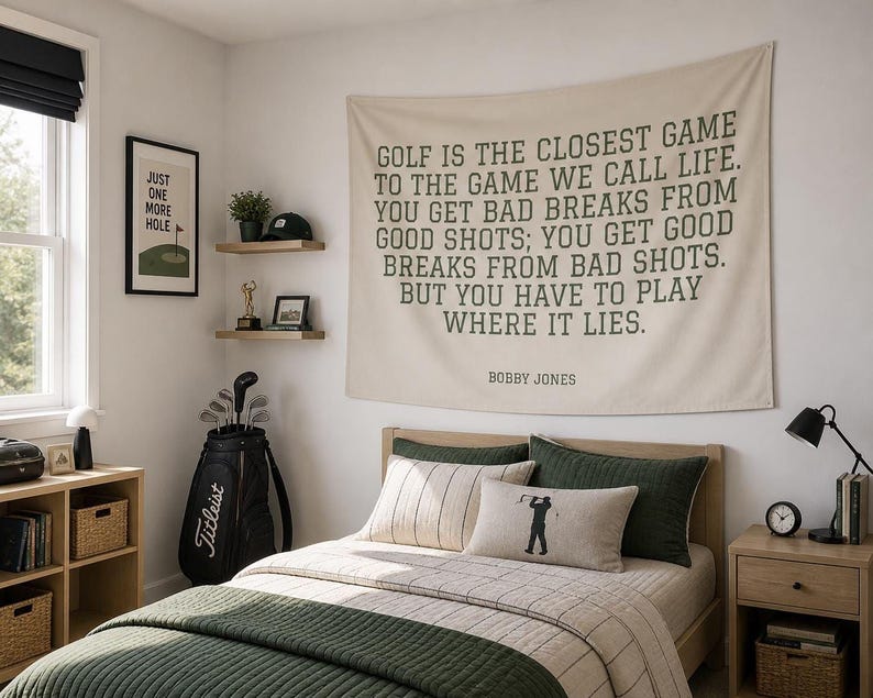 A bedroom with a large wall hanging featuring a quote about golf, a bed with a green blanket, a nightstand with a lamp, and shelves with various items.