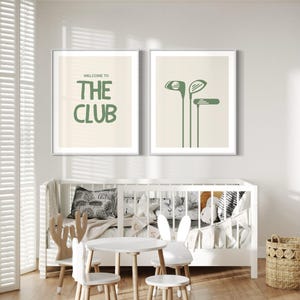 May include: Two framed prints with a white background and green text and illustrations. The first print says "Welcome to The Club" and the second print has three green golf clubs. The prints are hanging on a white wall above a white crib and a white table and chairs.