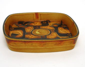 May include: A square ceramic dish with a brown glaze and a geometric design in black and yellow. The design features stylized birds and abstract shapes.
