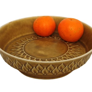 Op de afbeelding: Een bruine keramische kom met een zonnebloemdessin en een bladrand. Twee sinaasappels liggen in de kom.