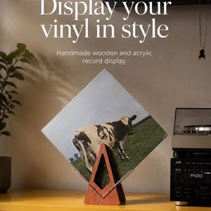 May include: A triangular wooden and clear acrylic record display stand holding a square vinyl record sleeve featuring a cow in a field. The text reads KoaWorksCo, Display your vinyl in style, and Handmade wooden and acrylic record display.