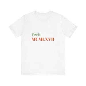 May include: White t-shirt with the text "Fecit: MCMILXXVII" printed in green and orange.