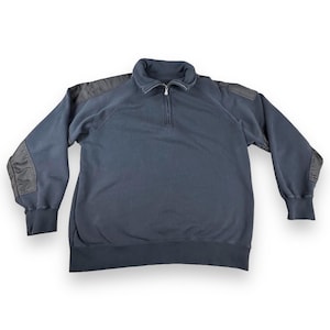 Könnte beinhalten: Ein marineblaues Sweatshirt mit einem Kragen mit Viertelreißverschluss und schwarzen Schulter- und Ellbogenpatches. Das langärmlige Oberteil hat gerippte Bündchen und eine lockere Passform.