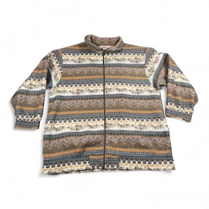 May include: A full-zip fleece jacket with a patterned design in shades of brown, tan, gray, and white. The jacket features a high collar and two front pockets. The pattern includes geometric and floral elements, creating a vintage aesthetic.