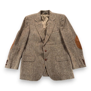 May include: A brown tweed blazer featuring a speckled pattern, notched lapels, and two front buttons. The jacket includes two flap pockets at the waist, brown suede elbow patches, and three small buttons on each sleeve cuff, with a smooth lining.
