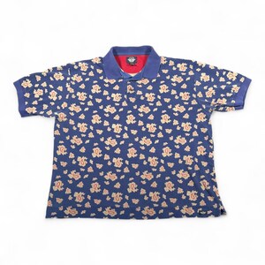 May include: A blue polo shirt with a paisley pattern in shades of tan and red. The shirt has a blue collar and short sleeves. The collar has a red lining and a logo. The shirt is made of a soft, comfortable material.