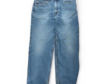 Puede incluir: Unos pantalones vaqueros azules con un diseño clásico de cinco bolsillos, cierre de botones y cintura de tiro medio. El tejido presenta un lavado medio con un ligero desgaste en los muslos y las rodillas, rematado con remaches de color cobre.