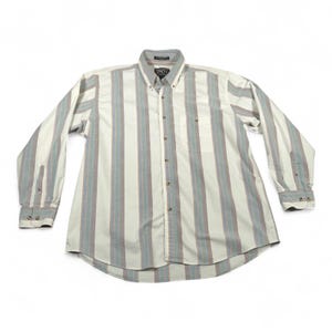 Puede incluir: Camisa abotonada de manga larga con rayas verticales en crema, azul y marrón. La camisa tiene cuello abotonado, bolsillo en el pecho y puños abotonados. La etiqueta dice "1857".