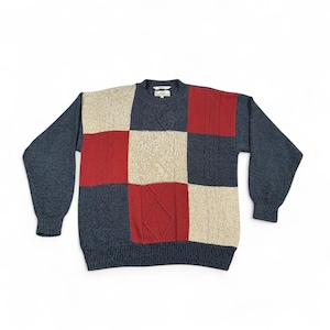 May include: A patchwork sweater in shades of navy blue, red, and beige. The sweater features a crew neck and long sleeves. The design is a mix of textured squares and knit patterns, creating a cozy and stylish look.