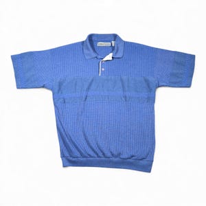 Peut inclure: Un polo bleu à manches courtes. La chemise a une texture côtelée et une bande horizontale contrastante sur la poitrine. Le col est d'une nuance de bleu plus claire et la chemise a une patte à deux boutons.