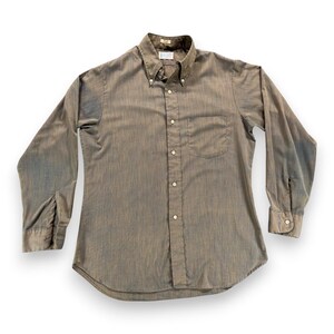 May include: A long-sleeve button-down shirt in a muted brownish-gray tone with a subtle vertical textured pattern. The shirt features a pointed collar with buttons, a single chest pocket on the left side, and white buttons running down the front placket.