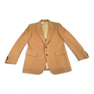 May include: A tan blazer featuring a two-button front closure, notched lapels, and two front flap pockets. The sleeves are finished with four small brown buttons at each cuff. The interior is lined with a light beige fabric featuring a repeating pattern.