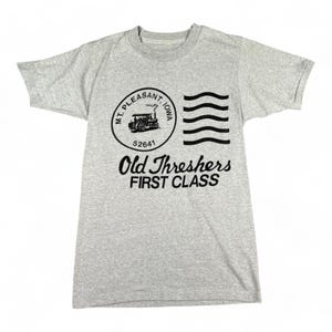 Può includere: T-shirt grigio chiaro con grafica circolare con la scritta "Mt. Pleasant, Iowa" e l'illustrazione di una locomotiva a vapore. Sotto la scritta "Old Threshers FIRST CLASS".