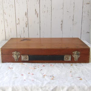May include: A rectangular wooden box with a dark brown finish. The box has metal clasps and a black leather handle. The box is sitting on a white surface.