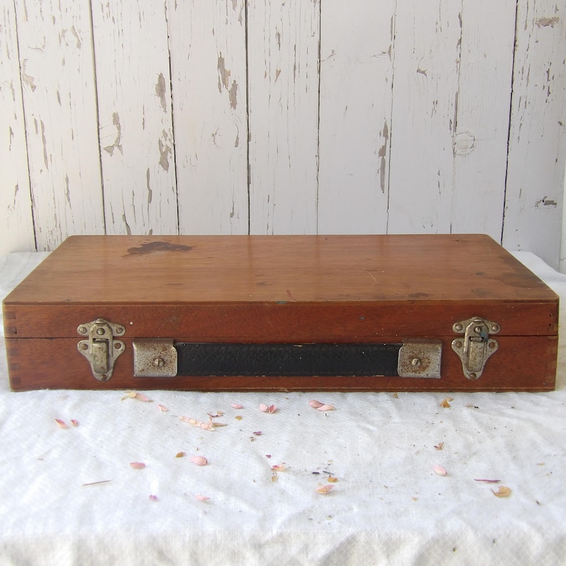 May include: A rectangular wooden box with a dark brown finish. The box has metal clasps and a black leather handle. The box is sitting on a white surface.