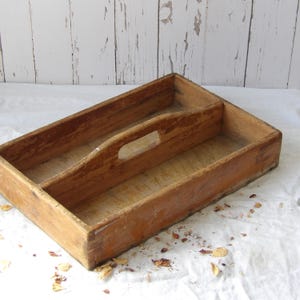 Può includere: Un vassoio rettangolare in legno con una finitura naturale color marrone chiaro e venature del legno visibili. Il vassoio presenta un divisorio centrale che corre lungo tutta la lunghezza, con una maniglia intagliata al centro.