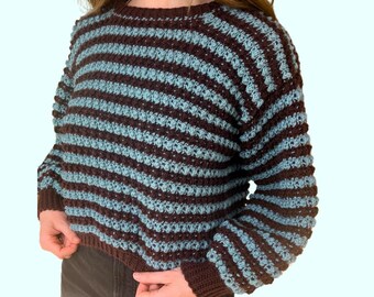 May include: A handmade crochet sweater with horizontal stripes in brown and light blue. The sweater has a crew neck and long sleeves with ribbed cuffs. The cropped style is visible in the image.