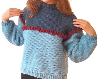 May include: A blue and burgundy crocheted sweater with a ruffled trim. The sweater has a high neck and long sleeves.