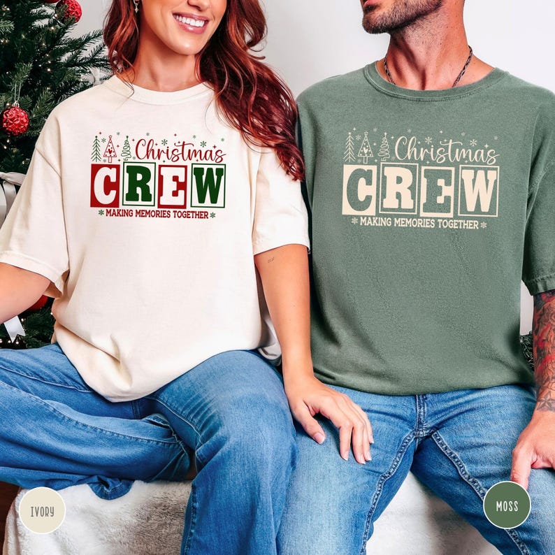 以下が含まれることがあります： 「Christmas CREW」の文字がデザインされた、アイボリーとモスグリーンの2枚のTシャツ。下には「MAKING MEMORIES TOGETHER」の文字。アイボリーのシャツはブルージーンズと組み合わせています。モスグリーンのシャツもブルージーンズと組み合わせています。