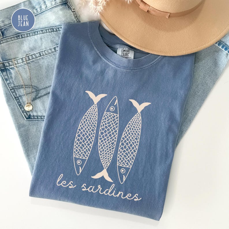 Op de afbeelding: Een blauw T-shirt met een witte afbeelding van drie gestileerde vissen en de tekst "les sardines".