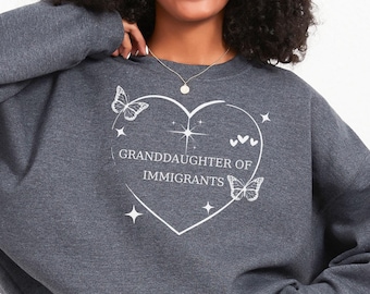 May include: A dark gray sweatshirt with a white heart graphic that says "Granddaughter of Immigrants" with butterflies and stars.