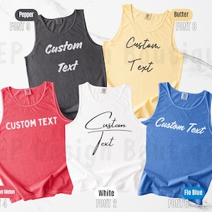 May include: Five sleeveless tank tops in pepper, butter, watermelon, white, and flo blue colors. Each tank top features the words Custom Text printed on the front in various fonts. The garments are displayed with labels indicating color and font style.