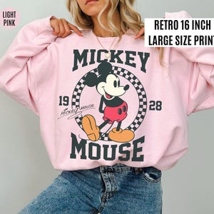Może przedstawiać: Jasnor&oacute;żowa bluza z nadrukiem w stylu retro z Myszki Miki. Grafika zawiera Myszkę Miki, napisy "Mickey Mouse" oraz lata "1928" i "19". Nadruk ma 40,6 cm.
