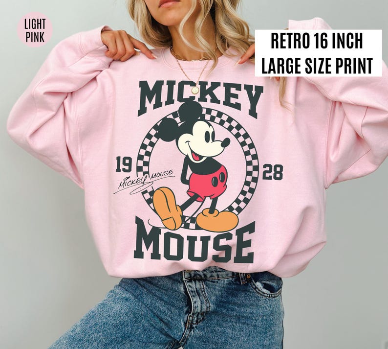 Może przedstawiać: Jasnor&oacute;żowa bluza z nadrukiem w stylu retro z Myszki Miki. Grafika zawiera Myszkę Miki, napisy "Mickey Mouse" oraz lata "1928" i "19". Nadruk ma 40,6 cm.