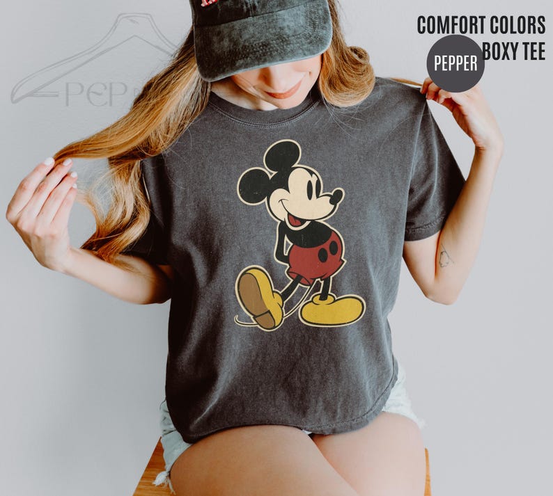 May include: Dark grey Comfort Colors boxy tee featuring a vintage Mickey Mouse graphic. The cartoon character is depicted in his classic pose, with red shorts, yellow shoes, and a smiling expression. The shirt has the text "COMFORT COLORS" and "BOXY TEE".