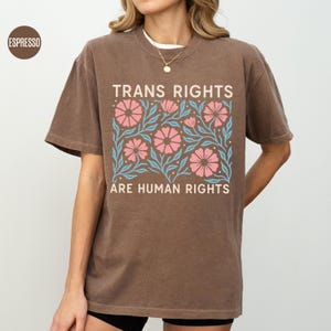May include: A brown t-shirt with a floral design and the text "Trans Rights Are Human Rights".