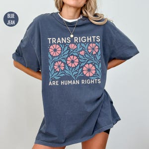 May include: A dark blue oversized t-shirt with a floral design and the text "Trans Rights Are Human Rights".