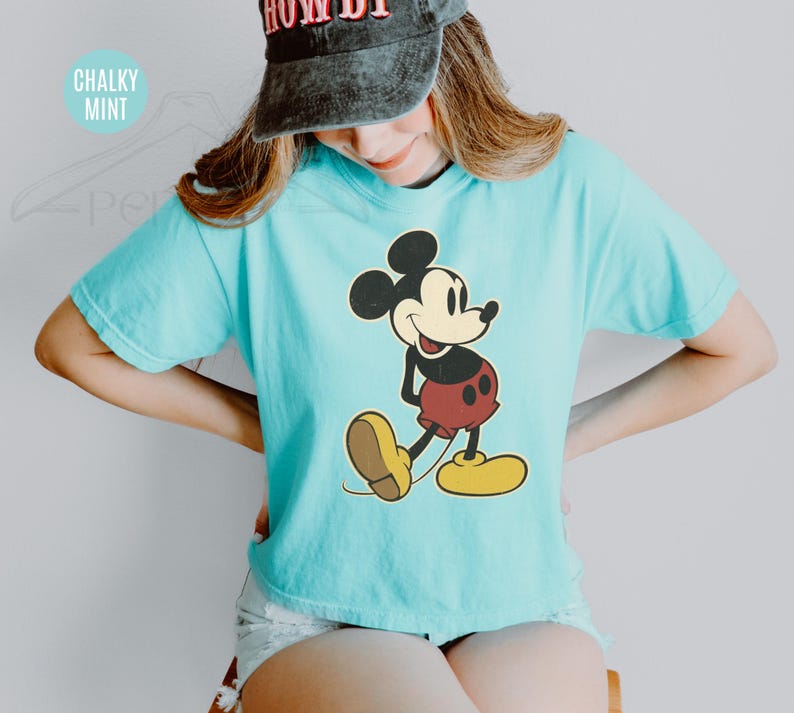 May include: A turquoise t-shirt with a Mickey Mouse design. The cartoon character is in black, red, yellow, and tan. The shirt has short sleeves and a loose fit. The text "Chalky Mint" is in the upper left corner.