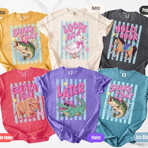 K&ouml;nnte beinhalten: Eine Auswahl an farbenfrohen T-Shirts in Gelb, Rot, Lila und Blau. Jedes Shirt zeigt ein einzigartiges Grafikdesign mit Text und Illustrationen von Tieren wie Fisch, Ente, Pferd, Alligator und B&uuml;ffel. Ma&szlig;e sind nicht relevant.