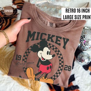 May include: Espresso-colored sweatshirt featuring a large Mickey Mouse graphic. The design includes the word "Mickey", the numbers "19" and "28", and the words "Mickey Mouse". The text "Retro 16 inch Large Size Print" is also visible.