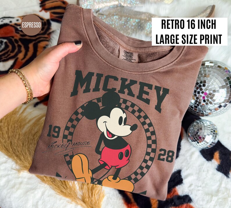May include: Espresso-colored sweatshirt featuring a large Mickey Mouse graphic. The design includes the word "Mickey", the numbers "19" and "28", and the words "Mickey Mouse". The text "Retro 16 inch Large Size Print" is also visible.