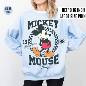 Może przedstawiać: Jasnoniebieska bluza z nadrukiem w stylu retro z Myszki Miki. Grafika przedstawia Myszkę Miki w czerwonych spodenkach i ż&oacute;łtych butach, z napisem "MICKEY MOUSE" i "Disney". Nadruk ma 40.6 cm.