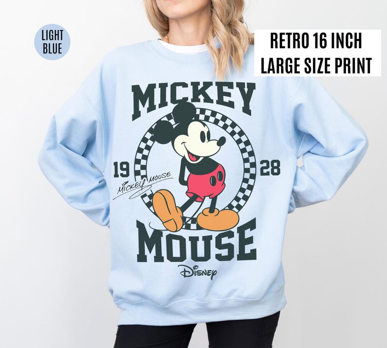 Może przedstawiać: Jasnoniebieska bluza z nadrukiem w stylu retro z Myszki Miki. Grafika przedstawia Myszkę Miki w czerwonych spodenkach i ż&oacute;łtych butach, z napisem "MICKEY MOUSE" i "Disney". Nadruk ma 40.6 cm.