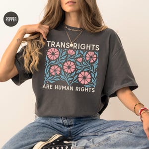 May include: A dark gray t-shirt with a floral design and the text "Trans Rights Are Human Rights".