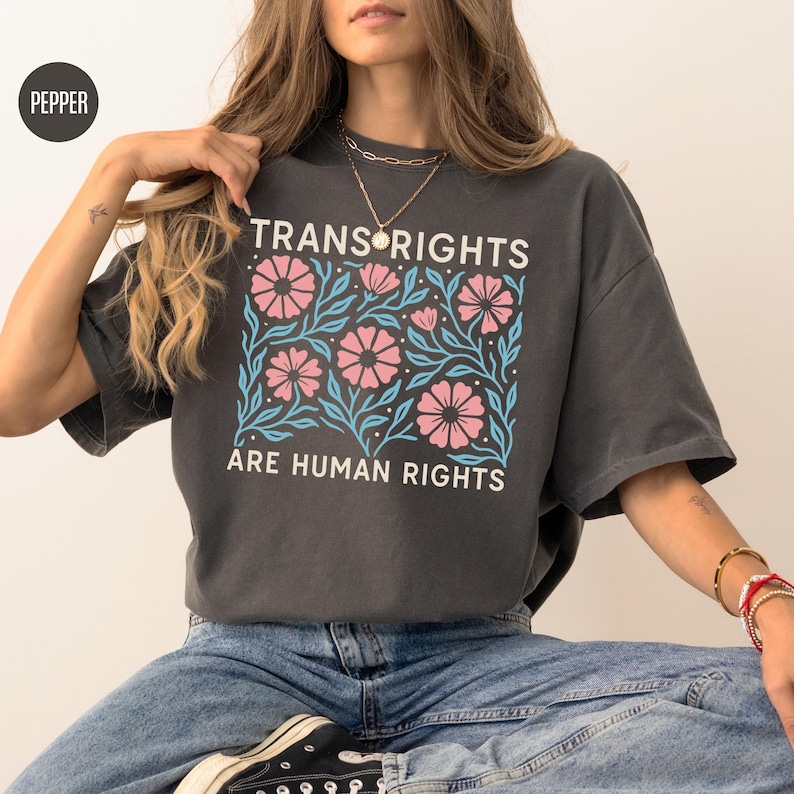 May include: A dark gray t-shirt with a floral design and the text "Trans Rights Are Human Rights".