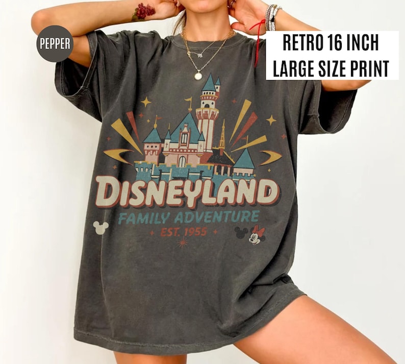 Puede incluir: Camiseta gris oscuro con un gr&aacute;fico de Disneyland. El gr&aacute;fico presenta un castillo, la palabra "Disneyland" y el texto "Family Adventure Est. 1955". La impresi&oacute;n mide 40.6 cm de ancho. La camiseta tiene mangas cortas.