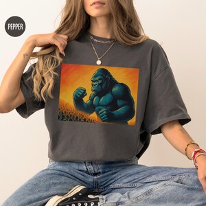 May include: A dark gray t-shirt with a graphic print of a large, muscular gorilla with a yellow background. The gorilla is in a fighting stance with its fists clenched.